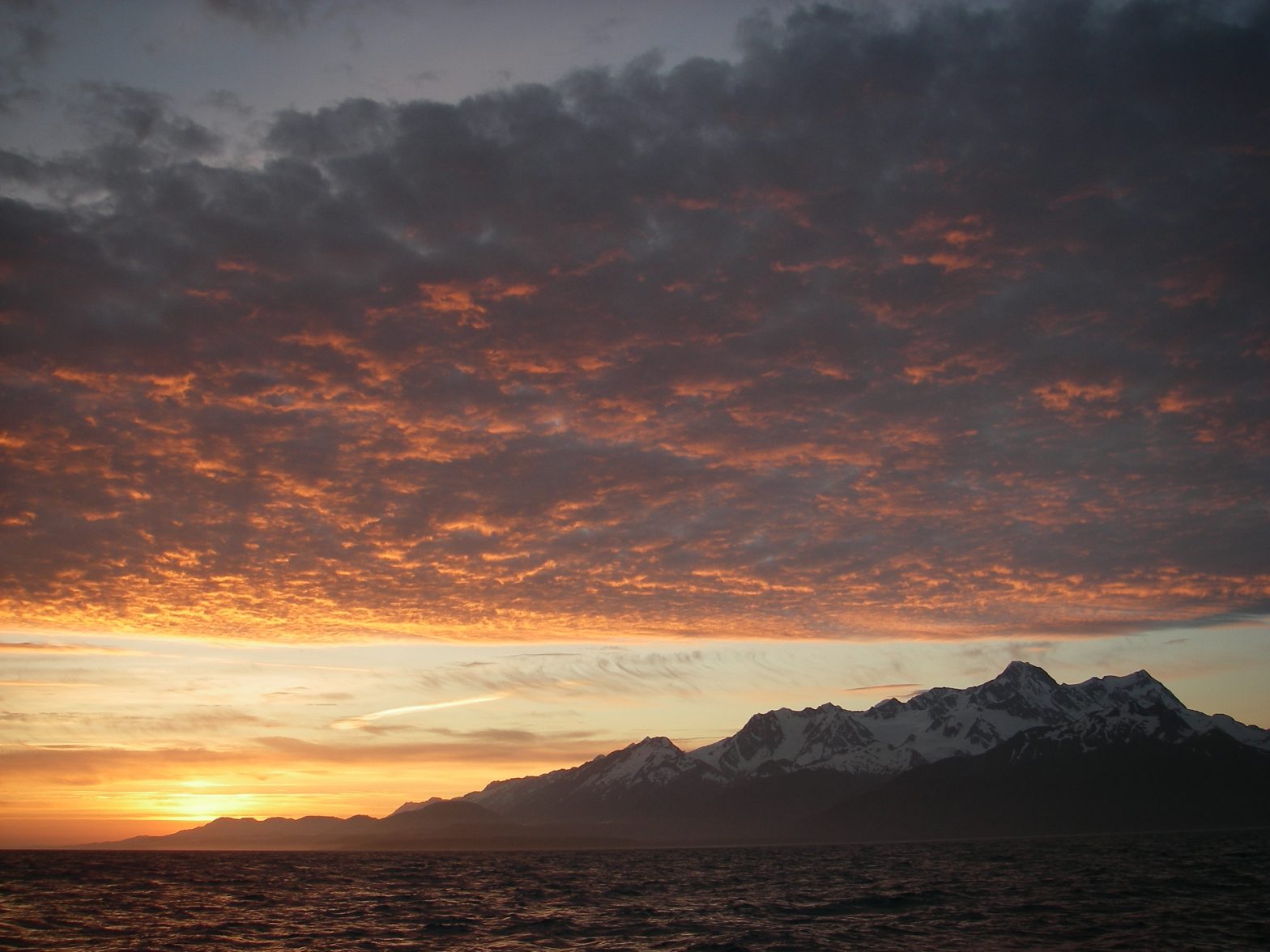 Sunset dropping behind snow covered mountain
